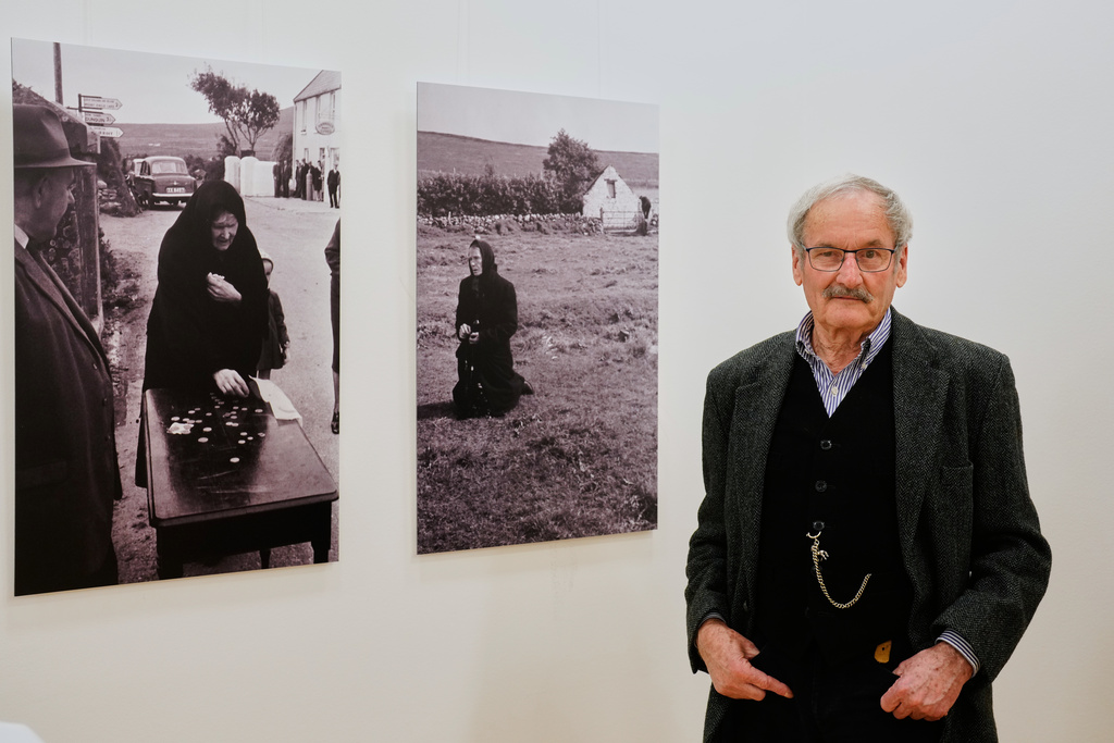 Diether Endlicher, a former photographer of The Associated Press, poses in front of pictures he took in Ireland in 1963 at his exhibition Ireland In The Frame at the Irish embassy in Berlin, Germany, Saturday, Nov. 22, 2025. (AP Photo/Markus Schreiber)