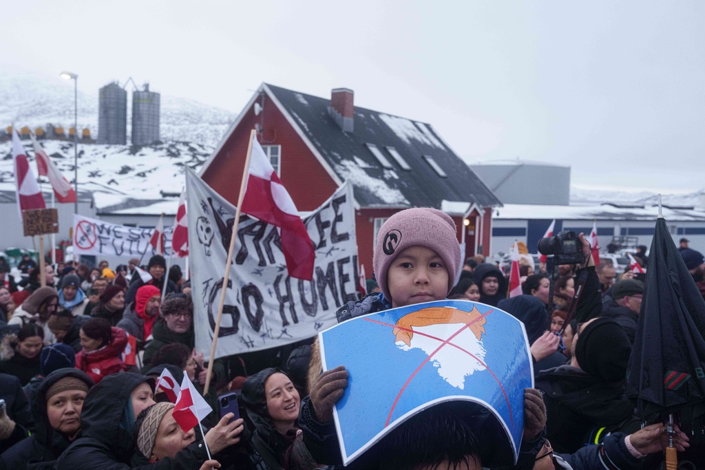 A boy holds a crossed out map of Greenland topped by a hairpiece symbolizing U.S. President Donald Trump, during a protest against Trump's policy towards Greenland in front of the US consulate in Nuuk, Greenland, Saturday, Jan. 17, 2026. (AP Photo/Evgeniy Maloletka)