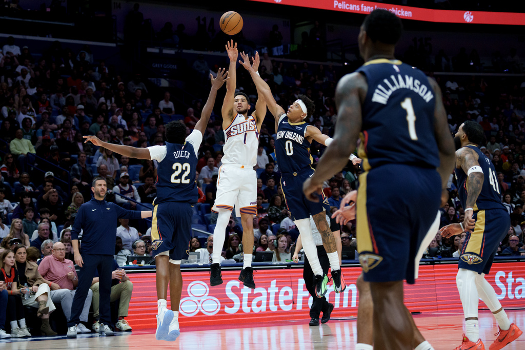 Phoenix Suns guard Devin Booker (1) shoots against New Orleans Pelicans center Derik Queen (22) and guard Jeremiah Fears (0) during the second half of an NBA basketball game in New Orleans, Saturday, Dec. 27, 2025. (AP Photo/Matthew Hinton)