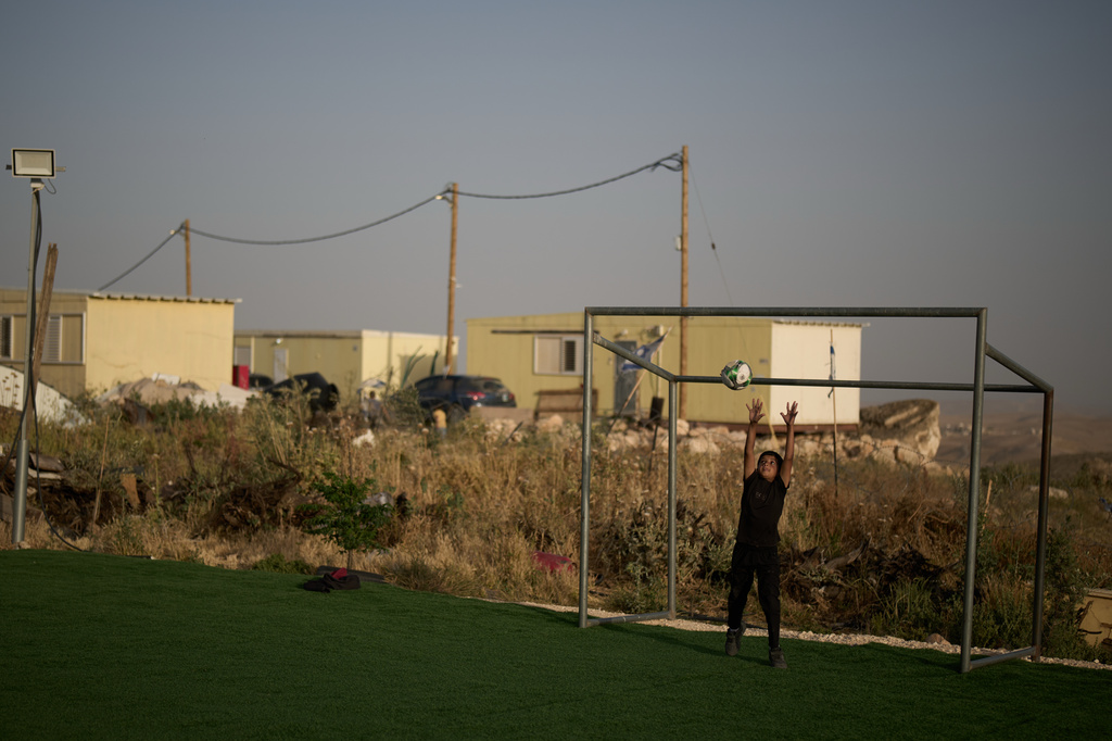 Backdropped by caravans from the Israeli settlement of Carmel, a Palestinian boy jumps for a ball while playing goalkeeper at a small soccer pitch in the West Bank Bedouin village of Umm al-Khair, Tuesday, May 12, 2026. (AP Photo/Leo Correa)
