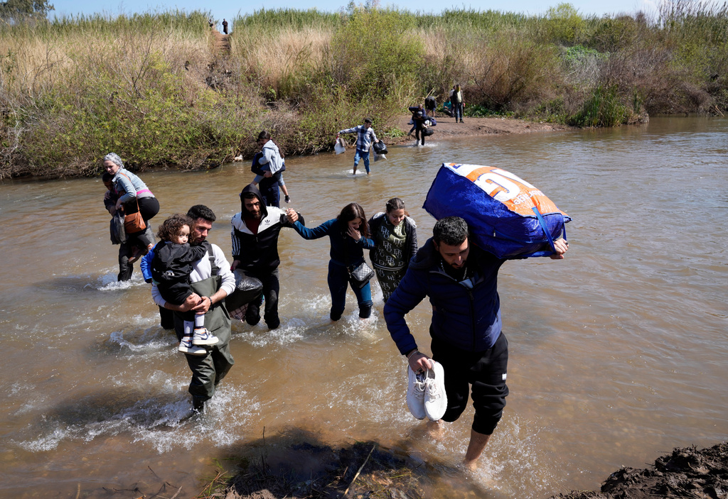 FILE - Syrian Alawite families who fled the clashes in Syria carry their luggage as they cross a river marking the border between Syria and northern Lebanon near the village of Heker al-Daher in Akkar province, Lebanon, March 11, 2025. (AP Photo/Hussein Malla, File)