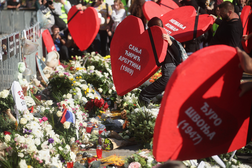 People place heart shaped banners carrying the names of the victims next to floral tributes outside the train station on the first anniversary of the disaster that killed 16 people, in Novi Sad, Serbia, Saturday, Nov. 1, 2025. (AP Photo/Armin Durgut)