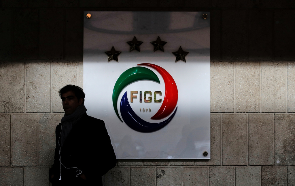 FILE - A journalist stands at the entrance of the FIGC Italian Soccer Federation, where a logo with four stars (one for each World Cup won) is seen partly in the shade, in Rome, on Nov. 14, 2017. (AP Photo/Alessandra Tarantino, File)