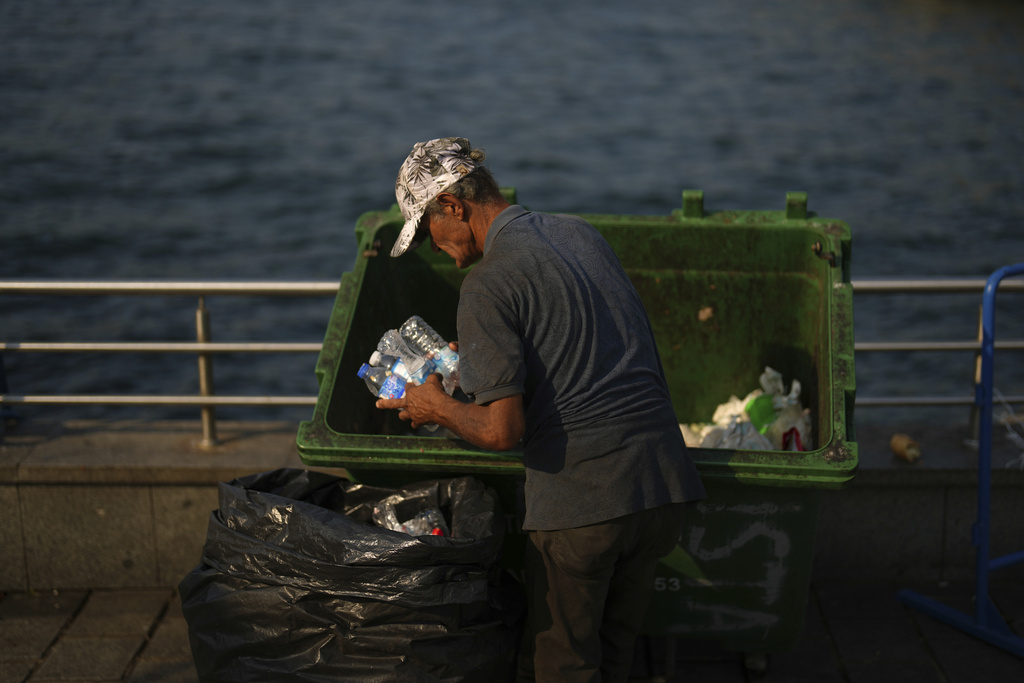 A garbage collector takes discarded plastic bottles from a street trash bin at Eminonu, in Istanbul, Turkey, Friday, Aug. 8, 2025. (AP Photo/Francisco Seco)