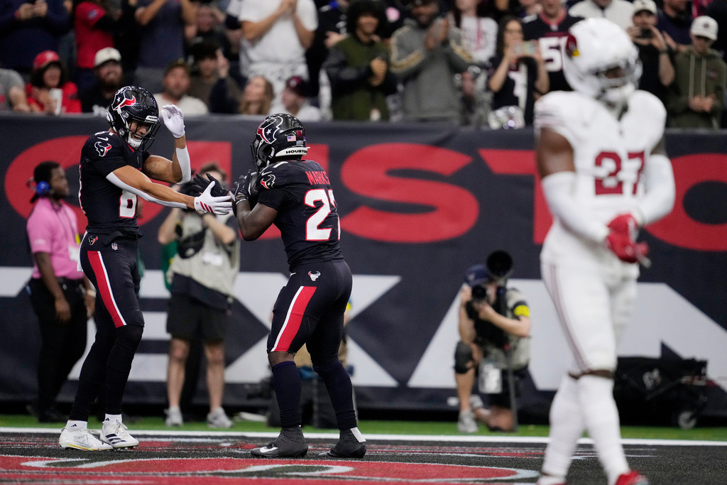 Houston Texans wide receiver Jayden Higgins, left, celebrates a Texans touchdown with Texans running back Woody Marks as Arizona Cardinals linebacker Akeem Davis-Gaither (27) pauses in the endzone during the first half of an NFL football game Sunday, Dec. 14, 2025, in Houston. (AP Photo/Ashley Landis)