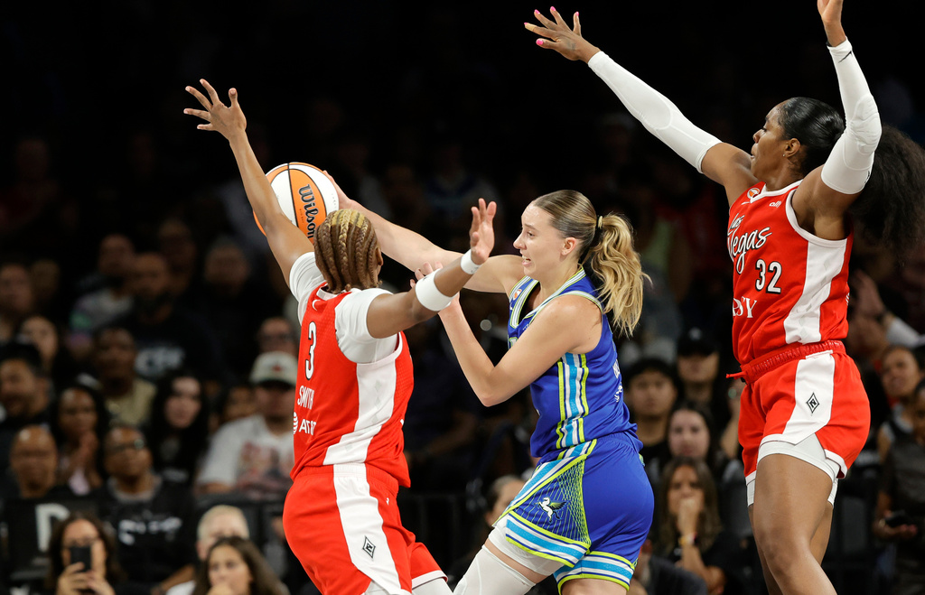 Dallas Wings guard Paige Bueckers, center, passes the ball between Las Vegas Aces forward NaLyssa Smith (3) and forward Cheyenne Parker-Tyus (32) during the first half of a WNBA basketball game Thursday, June 25, 2026, in Las Vegas. (Steve Marcus/Las Vegas Sun via AP)