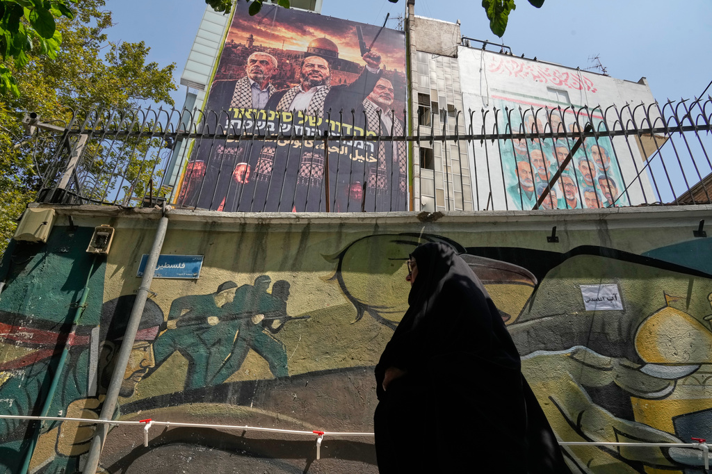A woman walks under a banner shows newly elected Hamas leader Khalil al-Hayya, center, alongside the late leaders Ismail Haniyeh, right, and Yahya Sinwar, with writing in Hebrew reads: "From Sinwar's generation, the new leader on the ground" and in Arabic: "Khalil al-Hayya, the occupiers' nightmare" at the Palestine square in downtown Tehran, Iran, Saturday, Aug. 1, 2026. (AP Photo/Vahid Salemi)
