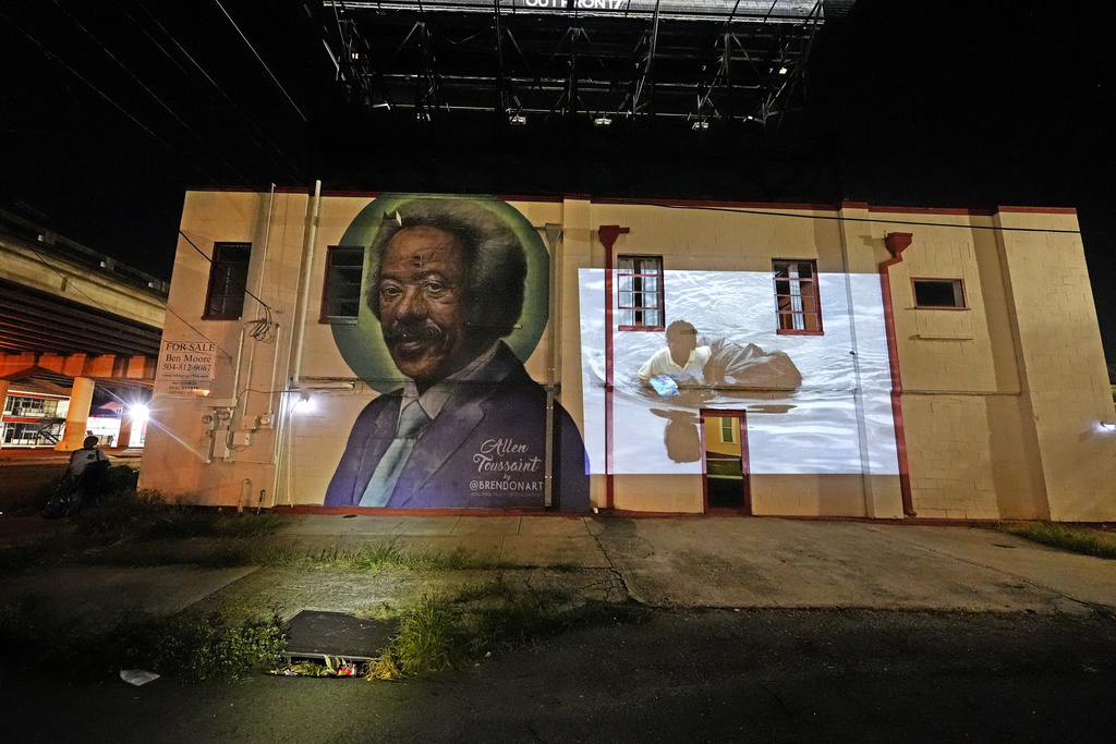 This photo of a young man wading through chest-deep floodwaters in the aftermath of Hurricane Katrina in New Orleans, taken by AP photographer Dave Martin, is projected Monday, Aug. 25, 2025, next to a mural of New Orleans music legend Allen Toussaint, below the overpass where the original photo was made. (AP Photo/Gerald Herbert)