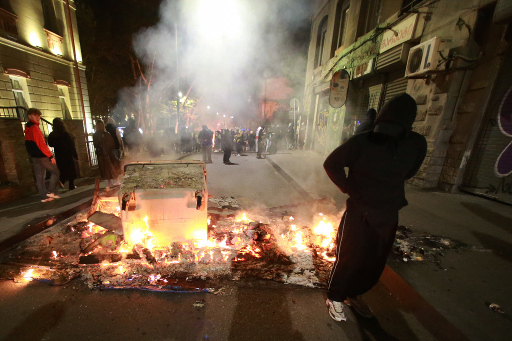 A demonstrator stands behind a burning barricade not far from a police line during an opposition rally in the city center of Tbilisi, Georgia, on Sunday, Oct. 5, 2025, boycotting the municipal elections and calling for the release of political opponents. (AP Photo/Zurab Tsertsvadze)