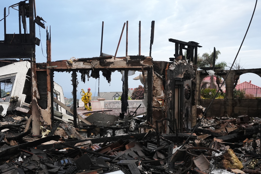 Firefighters gather hose among a destroyed home after the Norte Fire Saturday, Oct. 17, 2026, in San Juan Capistrano, Calif. (AP Photo/Gregory Bull)