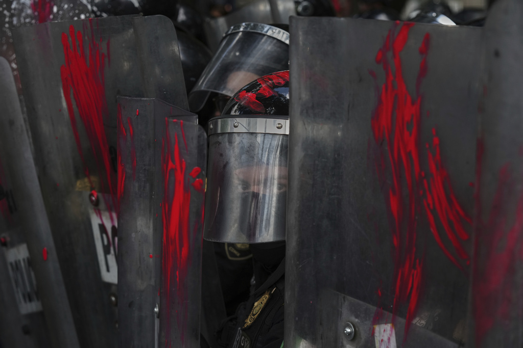 A police officer looks out from shields on which demonstrators smeared paint at a protest against the war in Gaza, in Mexico City, Sunday, Aug. 17, 2025. (AP Photo/Fernando Llano)