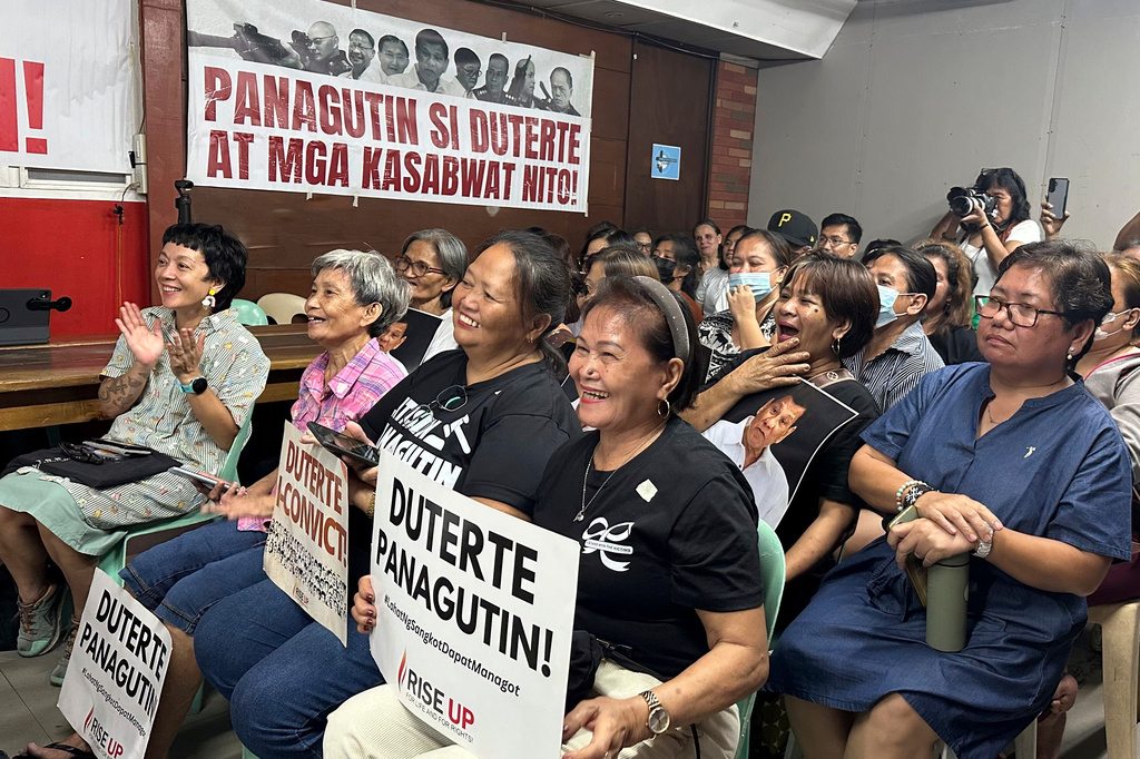 In this photo taken with a smartphone, families of victims of former Philippine President Rodrigo Duterte's war on drugs react as they watch him on a screen during a hearing at the International Criminal Court, in Manila, Philippines, Wednesday, Sept. 16, 2026. Banner seen In background reads "Hold Duterte and his accomplices accountable." (AP Photo/Joeal Calupitan)
