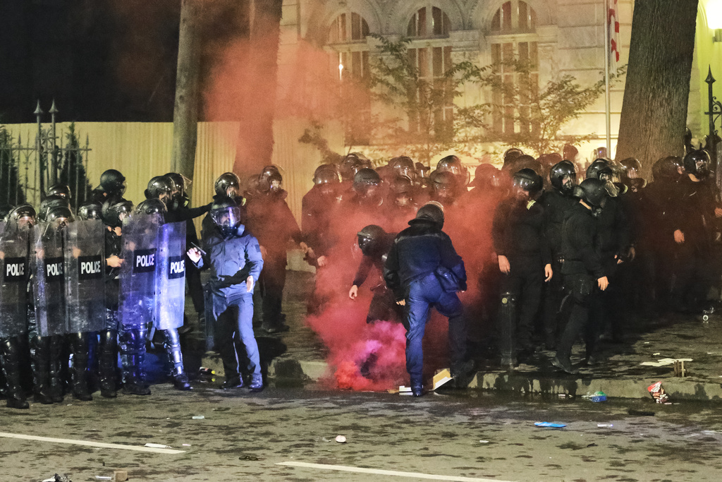 Police extinguish a flare thrown at them during an opposition rally in the city center of Tbilisi, Georgia, on Saturday, Oct. 4, 2025, boycotting the municipal elections and calling for the release of political opponents. (AP Photo/Zurab Tsertsvadze)