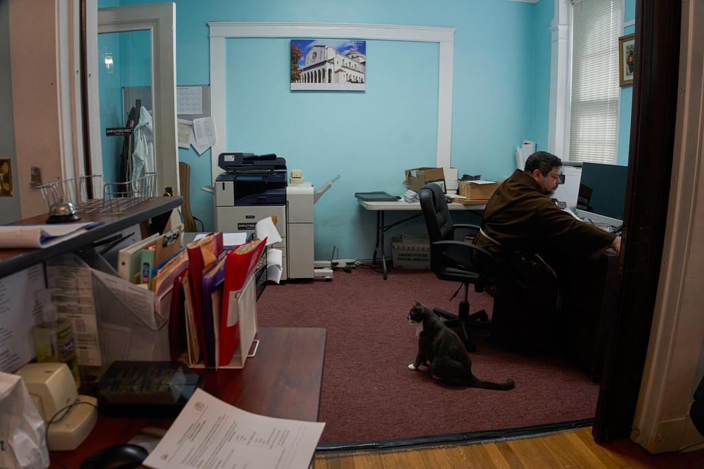 Reverend Carlos Reyes works in the office of the Shrine of the Sacred Heart as the parish cat, Maseo, named after Friar Masseo, a close companion of St. Francis, in Washington, Oct. 12, 2025. (AP Photo/Luis Andres Henao)