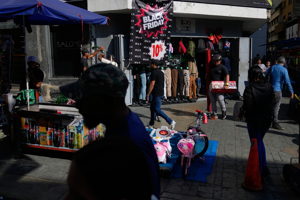 Pedestrians walk past a storefront promoting Black Friday discounts in Caracas, Venezuela, Friday, Nov. 28, 2025. (AP Photo/Ariana Cubillos)