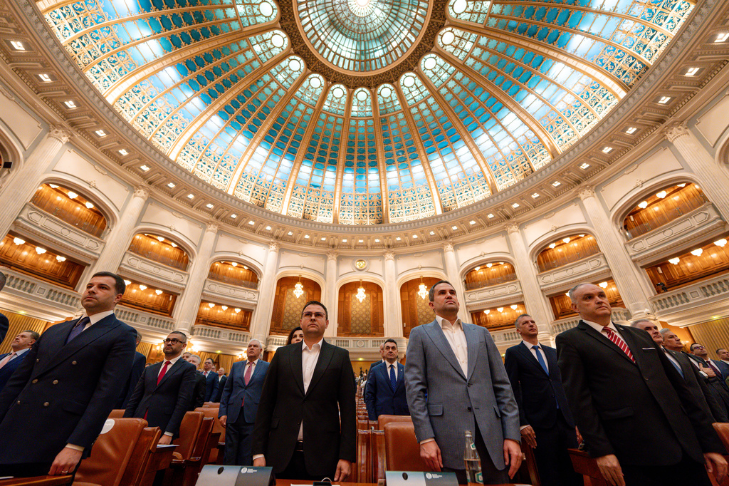 Romanian lawmakers stand during the anthem ahead of a no confidence vote against Prime Minister Ilie Bolojan's government in Romania's parliament in Bucharest, Romania, Tuesday, May 5, 2026. (AP Photo/Vadim Ghirda)