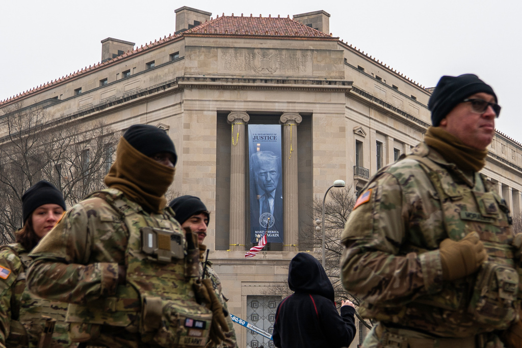 Members of the National Guard walk past a banner with President Donald Trump hanging on the Department of Justice, Thursday, Feb. 19, 2026, in Washington. (AP Photo/Allison Robbert)