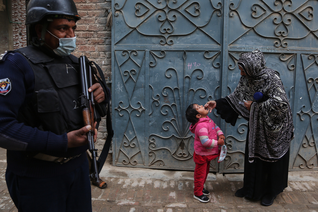 A police officer stands guard as a health worker, right, administers a polio vaccine to a child at a neighbourhood in Peshawar, Pakistan, Monday, Monday, Dec. 15, 2025. (AP Photo/Muhammad Sajjad)