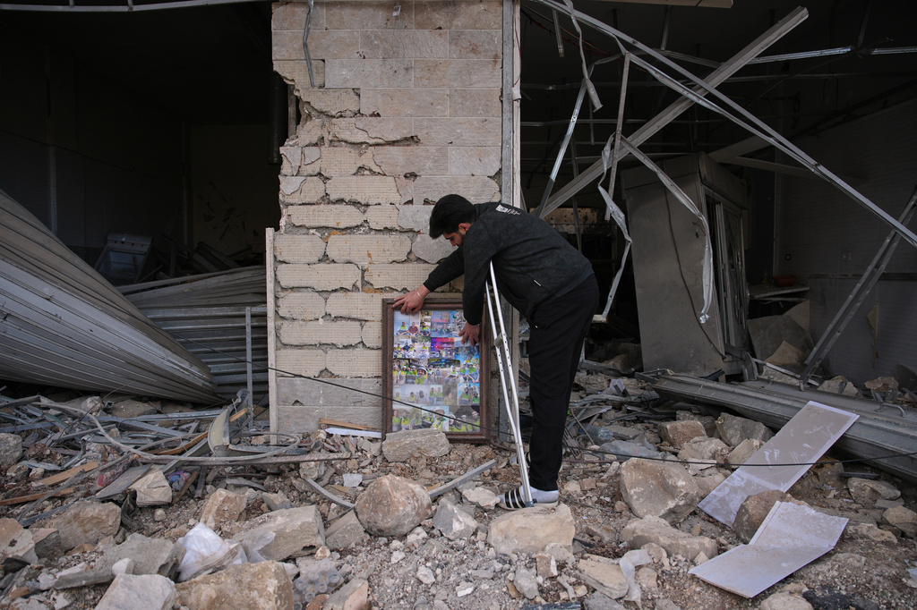 A Hezbollah health unit member Ali Fahos places portraits of his colleagues, killed during the previous war with Israel, next to a building destroyed in an Israeli airstrike in Jibchit, southern Lebanon, Friday, April 17, 2026, following a ceasefire between Israel and Hezbollah. (AP Photo/Hassan Ammar)