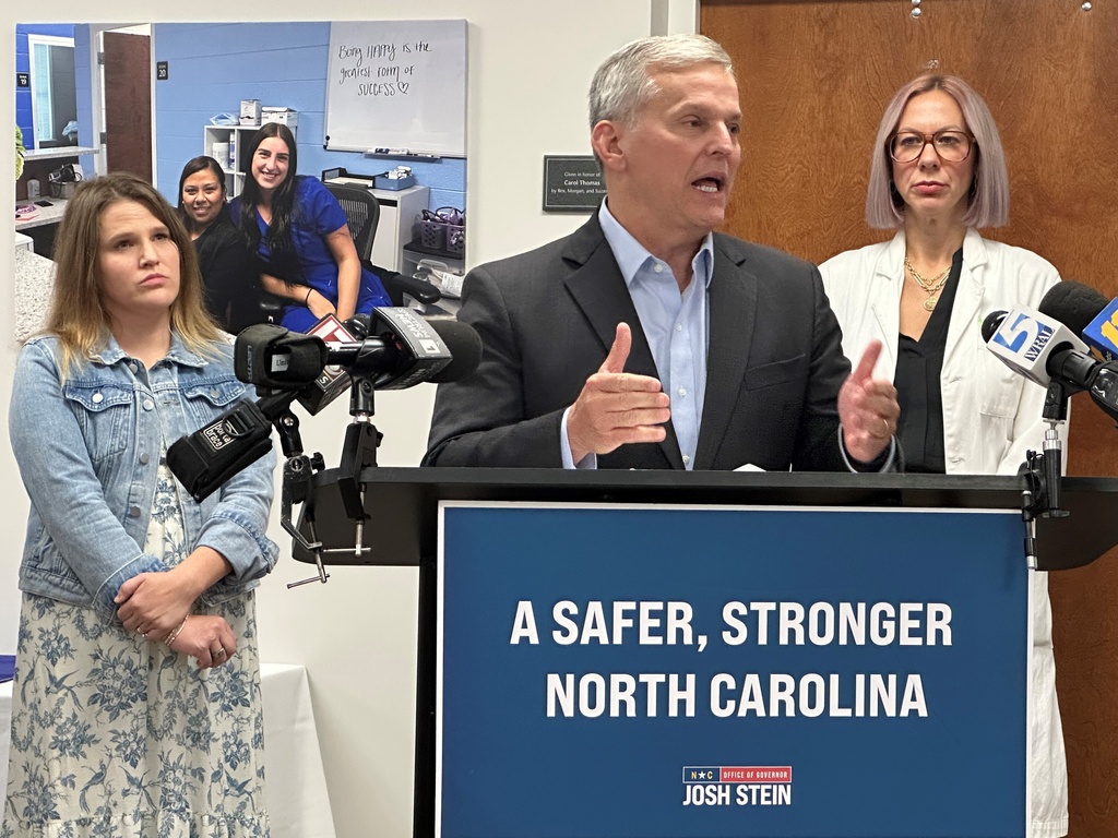 North Carolina Gov. Josh Stein speaks while Chelsea Gray of Rutherfordton, N.C., left, and Dr. Jenna Beckham, right, listen at a news conference about Medicaid reimbursement rate reductions at the Alliance Medical Ministry in Raleigh, N.C., on Thursday, Sept. 25, 2025 (AP Photo/Gary D. Robertson)
