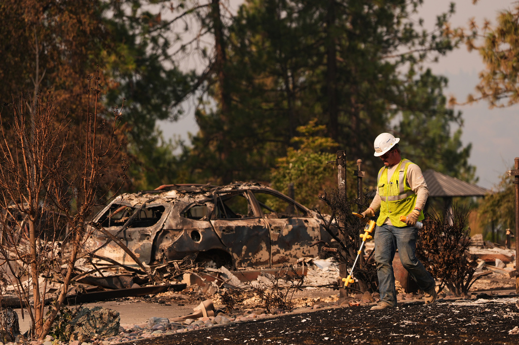 A worker with Avista moves through a property after a wildfire hit the northern part of Spokane, Wash., Monday, Aug. 3, 2026. (AP Photo/Lindsey Wasson)