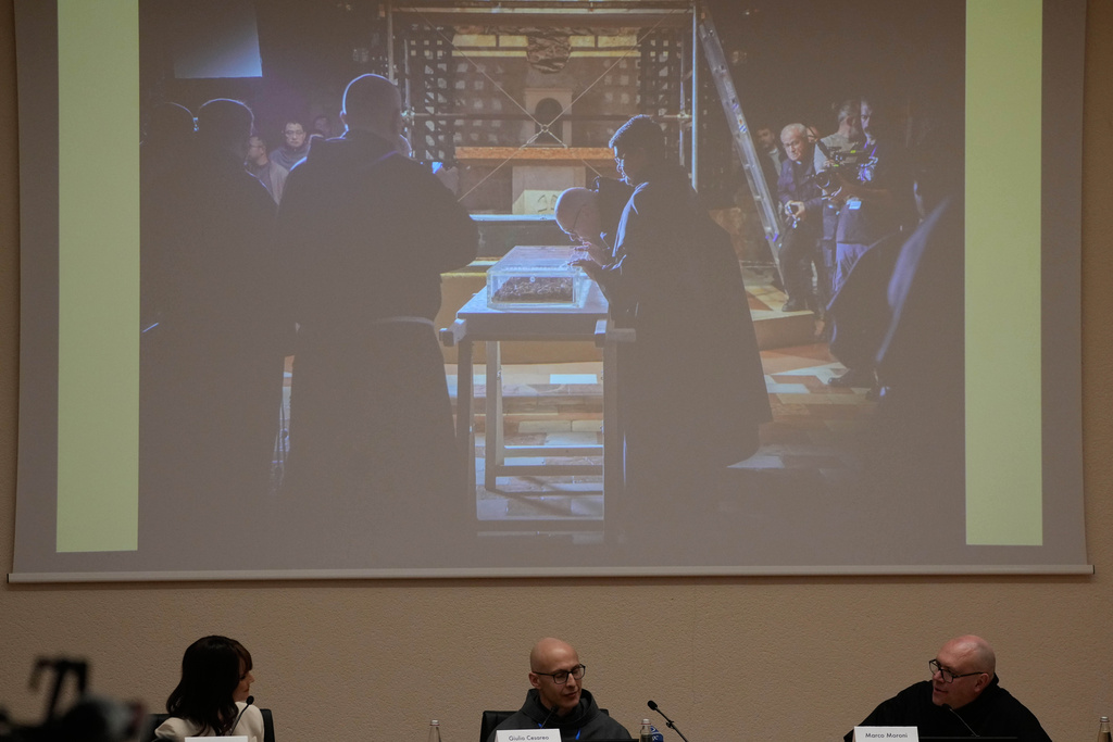 From left, TV Lorena Bianchetti, Friar Giulio Cesareo director of the communications office of the Basilica of St. Francis, and Friar Marco Moroni, Custodian of the Sacred Convent, show journalists the the moment when the saint's bones were extracted from the reliquary in Assisi, Italy, Saturday, Feb. 21, 2026, on the eve of the public display of St. Francis' remains to mark the 800th anniversary of his death in 1226.(AP Photo/Gregorio Borgia)