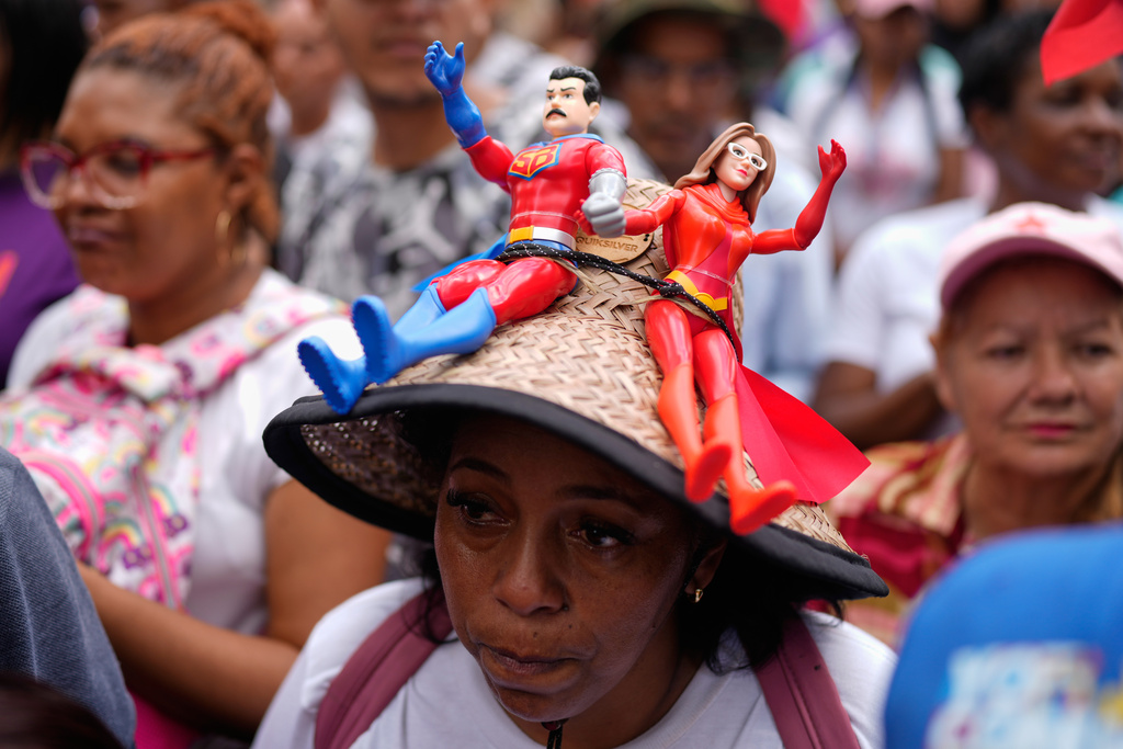 A government supporter wears a hat with dolls from the TV program, Super Bigote, based on President Nicolas Maduro and first lady Cilia Flores, during a protest demanding their release from U.S. custody, in Caracas, Venezuela, Sunday, Jan. 4, 2026. (AP Photo/Ariana Cubillos)