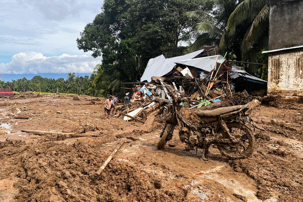 Th wreckage of a motorcycle is seen caked in mud as people inspect the ruin of a house at a village affected by a flash flood in Agam, West Sumatra, Indonesia, Sunday, Nov. 30, 2025. (AP Photo/Ade Yuandha)