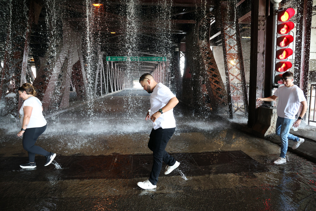 People scamper west across the lower level of the DuSable Lake Shore Drive bridge over the Chicago River on Wednesday, Sept. 2, 2026, as water pumped by a Chicago Fire Department boat flows down onto the double-leaf, double-deck, fixed counterweight bridge. (Terrence Antonio James/Chicago Tribune via AP)