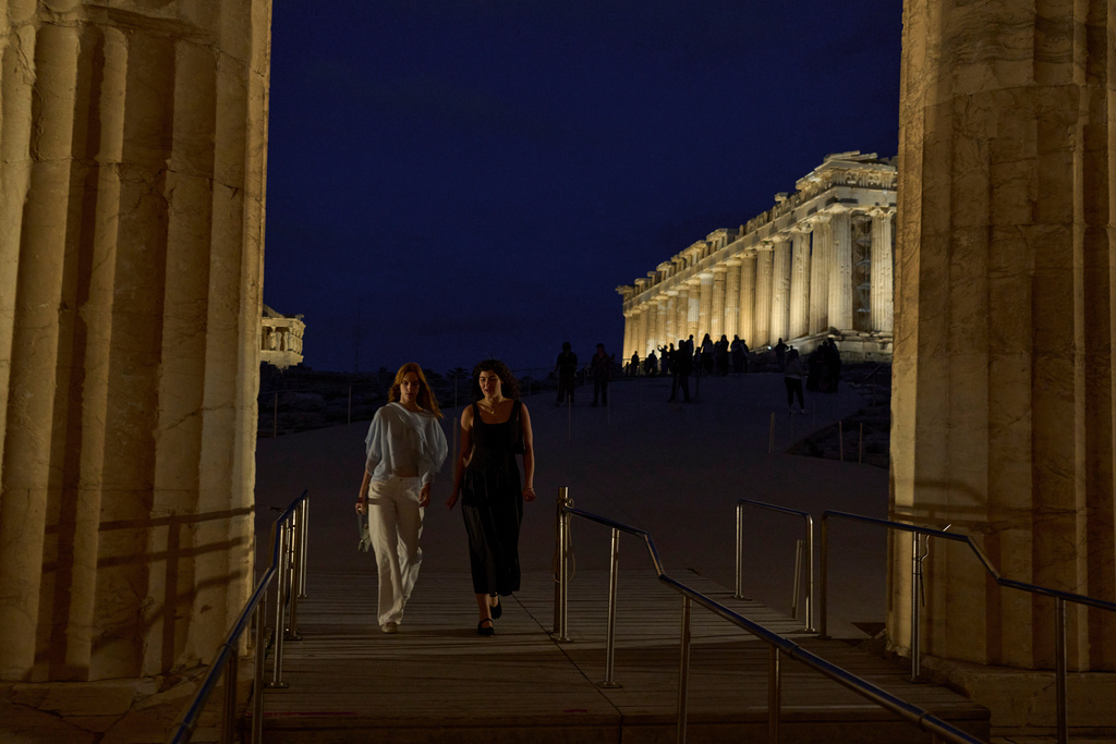 Tourists walk in front of the illuminated 5th century B.C. Parthenon atop the Acropolis hill in Athens, Friday, Oct. 31, 2025. (AP Photo/Petros Giannakouris)