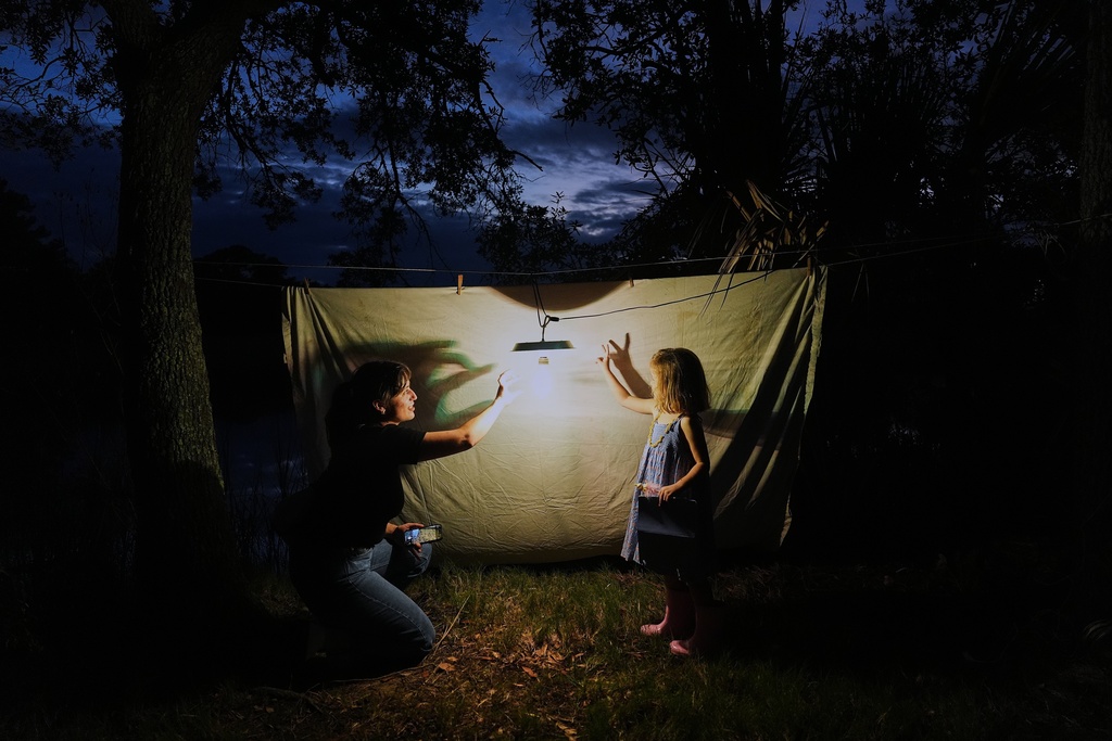 Schuyler Clogston, left, makes shadows puppets with Agnes Suárez after setting up a sheet and light to attract moths for observation Tuesday, Oct. 7, 2025, in Charleston, S.C. (AP Photo/Joshua A. Bickel)