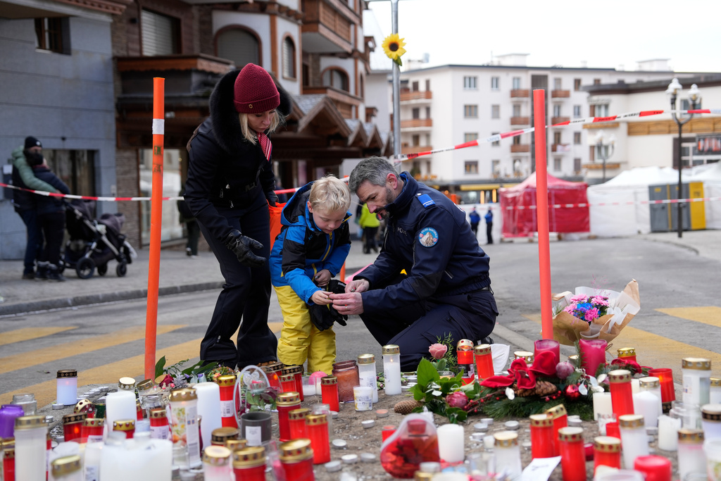 A police officer helps a boy to light a candle near the sealed off Le Constellation bar in Crans-Montana, Swiss Alps, Switzerland, Friday, Jan. 2, 2026, where a devastating fire left dead and injured during the New Year's celebrations. (AP Photo/Baz Ratner)