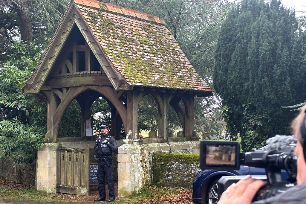 A camera man films a police officer guarding the entrance to Churchyard of the Sandringham Royal Estate in Sandringham, Thursday, Feb. 19, 2026 after Andrew Mountbatten-Windsor has been arrested by British police on suspicion of misconduct in public office. (AP Photo/Matthew Kemp)