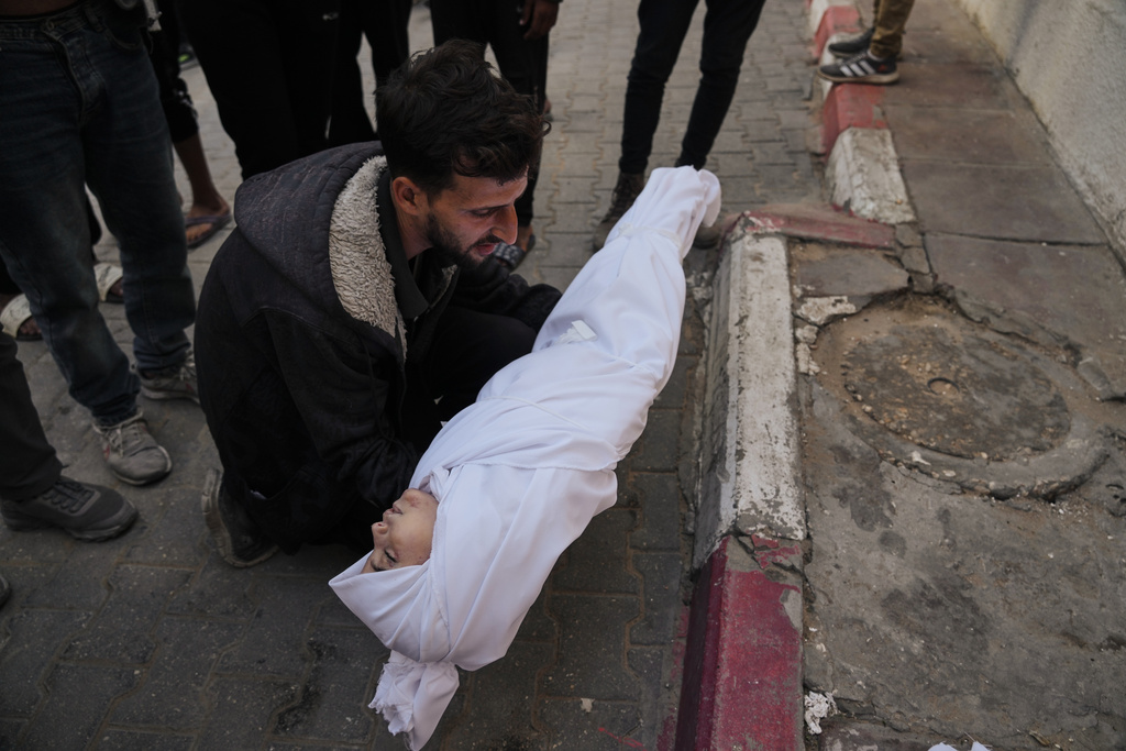 A man carries the body of a child from the Azzam family, killed in Israeli strikes, during her funeral at Shifa Hospital in Gaza City Thursday, Nov. 20, 2025. (AP Photo/Jehad Alshrafi)