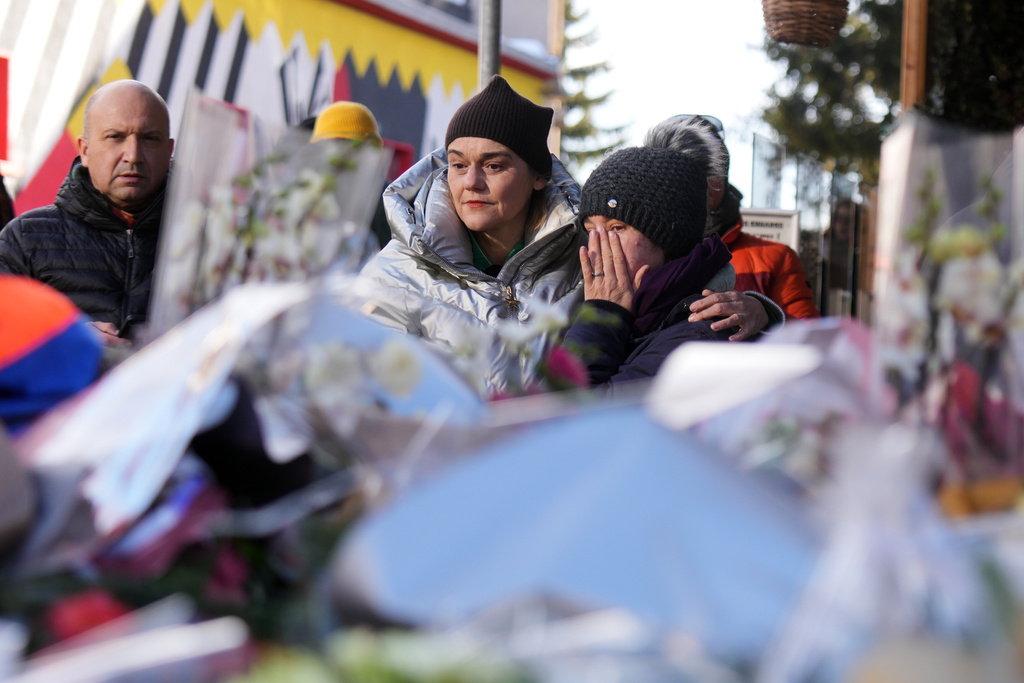 People mourn behind flowers and letters near the sealed off Le Constellation bar, where a devastating fire left dead and injured during the New Year's celebrations in Crans-Montana, Swiss Alps, Switzerland, Friday, Jan. 2, 2026. (AP Photo/ Antonio Calanni)