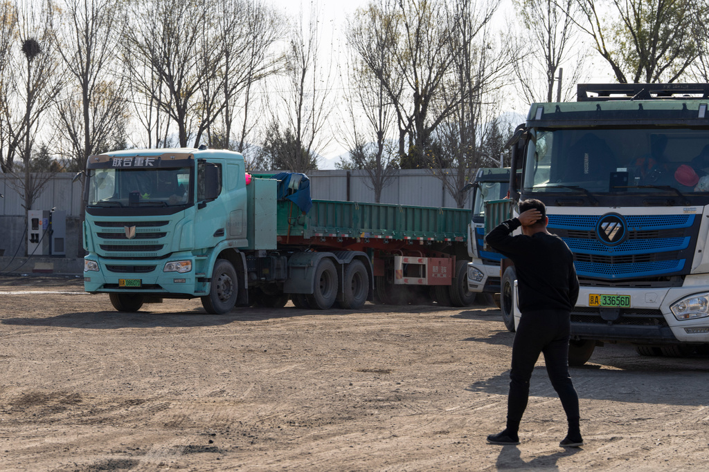 A driver walks past electric trucks at a charging station on the outskirts of Beijing, on Nov. 14, 2025. (AP Photo/Ng Han Guan)