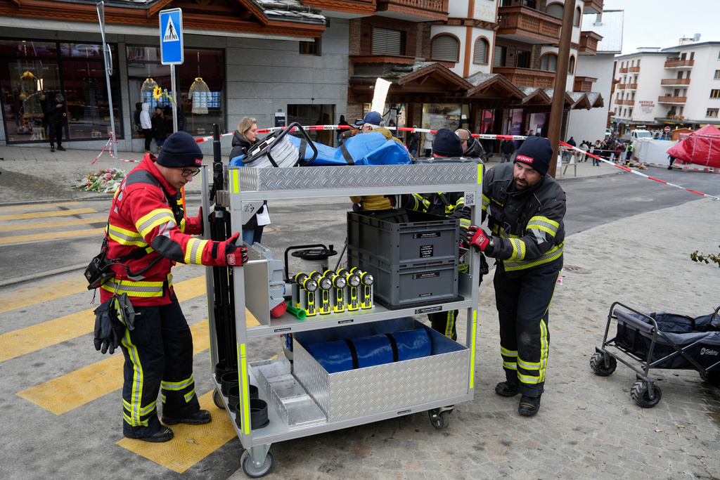 Firefighters pull a trolley with equipment near the sealed off Le Constellation bar in Crans-Montana, Swiss Alps, Switzerland, Friday, Jan. 2, 2026, where a devastating fire left dead and injured during the New Year's celebrations. (AP Photo/Baz Ratner)