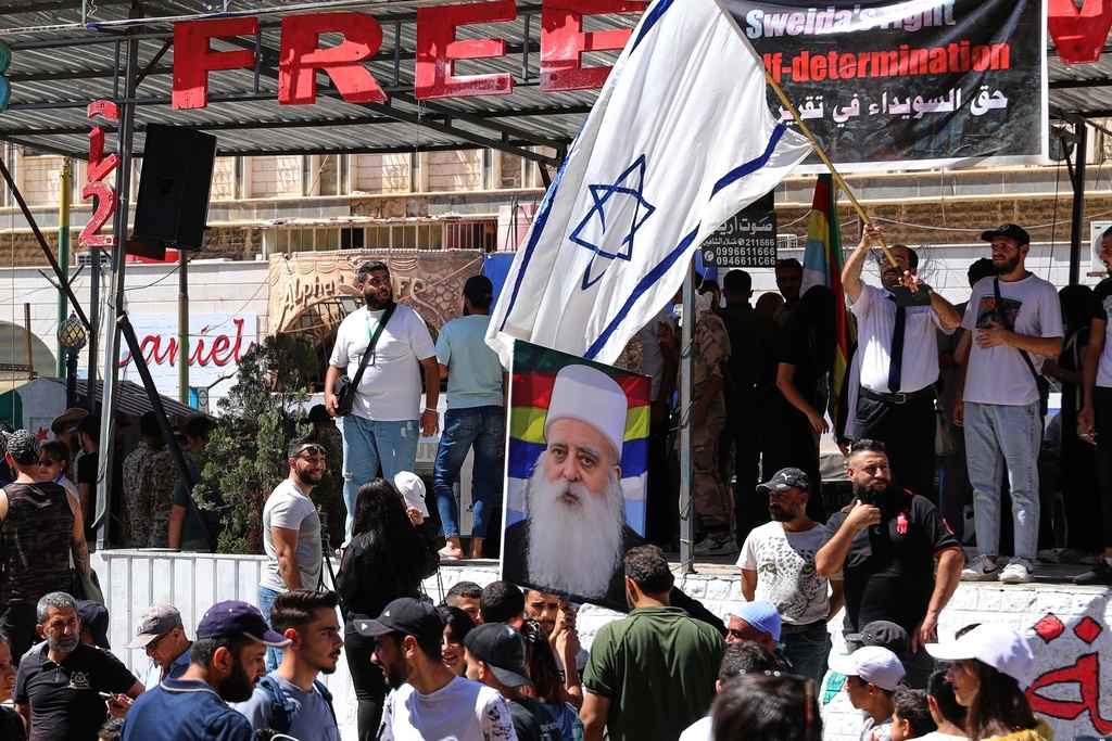 FILE - A man waves an Israeli flag over a picture of Sheikh Mowafak Tarif, the spiritual leader of the Druze in Israel, during a weekly rally in Sweida, southern Syria, on Sept. 20, 2025. (AP Photo/Fahd Kiwan, File)
