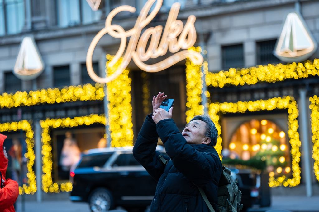 A man takes a photo of Rockefeller Center in front of Saks Fifth Avenue on Black Friday in New York on Friday, Nov. 28, 2025. (AP Photo/Angelina Katsanis)