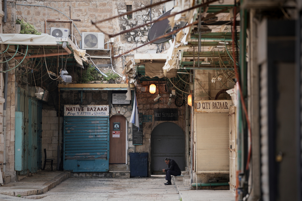 A man sits beside a locked door of the Church of the Holy Sepulchre and shuttered shops in Jerusalem’s Old City, which remains off limits to visitors amid the war with Iran, Friday, March 27, 2026. (AP Photo/Mahmoud Illean)