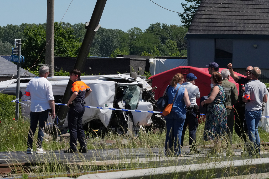Police and residents gather around a level crossing where a train collided with a van in Buggenhout, Belgium, Tuesday, May 26, 2026. (AP Photo/Marius Burgelman)
