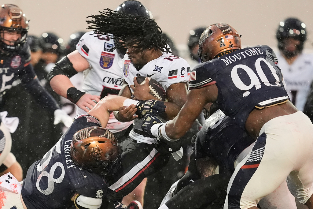 Cincinnati running back Zion Johnson (13) loses his helmet as he tackled by Navy linebacker Coleman Cauley (58) and defensive end Julien Moutome (90) during the first half of the Liberty Bowl NCAA college football game Friday, Jan. 2, 2026, in Memphis, Tenn. (AP Photo/George Walker IV)