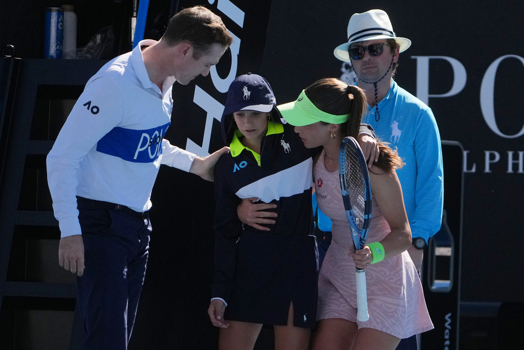 Zeynep Sonmez of Turkey and umpire Chase Urban help a ball kid who fainted, from the court during her first round match against Ekaterina Alexandrova of Russia at the Australian Open tennis championship in Melbourne, Australia, Sunday, Jan. 18, 2026. (AP Photo/Asanka Brendon Ratnayake)