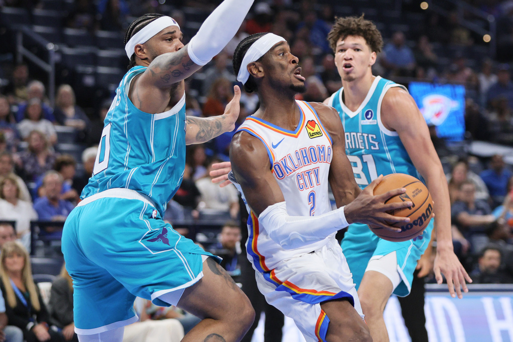Oklahoma City Thunder guard Shai Gilgeous-Alexander, center, looks to pass the ball away from Charlotte Hornets forwards Miles Bridges, left, and Tidjane Sala&uuml;n, right, during the first half of a preseason NBA basketball game Thursday, Oct. 9, 2025, in Oklahoma City. (AP Photo/Nate Billings)