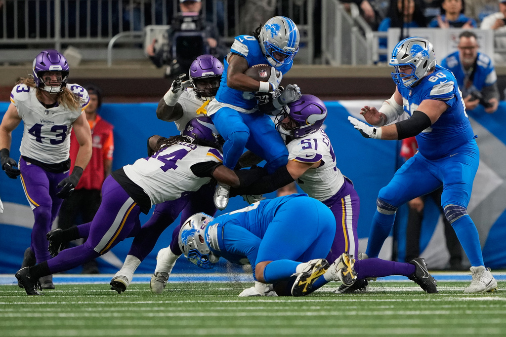 Detroit Lions running back Jahmyr Gibbs (0) is tackled by Minnesota Vikings safety Josh Metellus (44) and linebacker Blake Cashman (51) during the second half of an NFL football game Sunday, Nov. 2, 2025, in Detroit. (AP Photo/Ryan Sun)