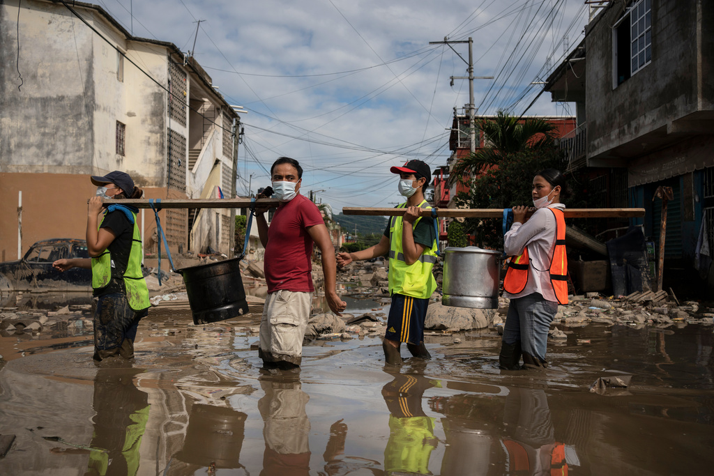 Locals carry pots of tamales donated by volunteers to victims of torrential rain through a flooded street in Poza Rica, Veracruz state, Mexico, Wednesday, Oct. 15, 2025. (AP Photo/Felix Marquez)