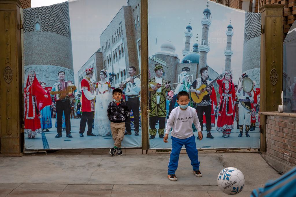 FILE - Children play soccer in front of a gate with a mural depicting Uyghur musicians at the International Grand Bazaar in Urumqi in western China's Xinjiang Uyghur Autonomous Region, as seen during a government organized trip for foreign journalists, April 21, 2021. (AP Photo/Mark Schiefelbein, File)