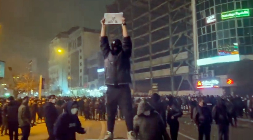 In this frame grab from video obtained by the AP outside Iran, a masked demonstrator holds a picture of Iran's Crown Prince Reza Pahlavi during a protest in Tehran, Iran, Friday, January. 9, 2026. (UGC via AP)