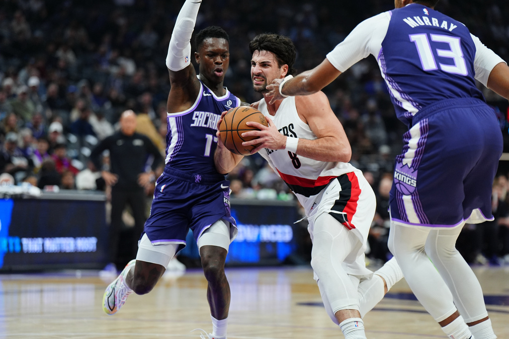 Portland Trail Blazers forward Deni Avdija (8) drives between Sacramento Kings guard Dennis Schroder, left, and forward Keegan Murray (13) during the first half of an NBA basketball game Saturday, Dec. 20, 2025, in Sacramento, Calif. (AP Photo/Alan Greth)