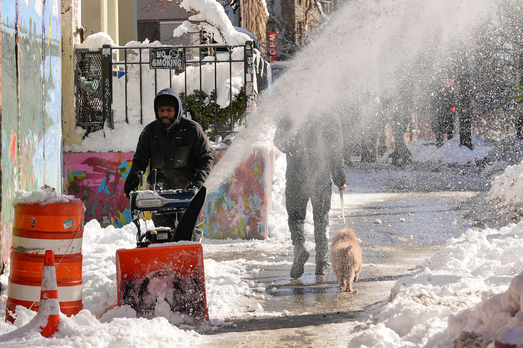 A worker uses a snow blower to clear snow from a sidewalk in front of retail shops, Tuesday, Feb. 24, 2026, in the Brooklyn borough of New York. (AP Photo/Yuki Iwamura)